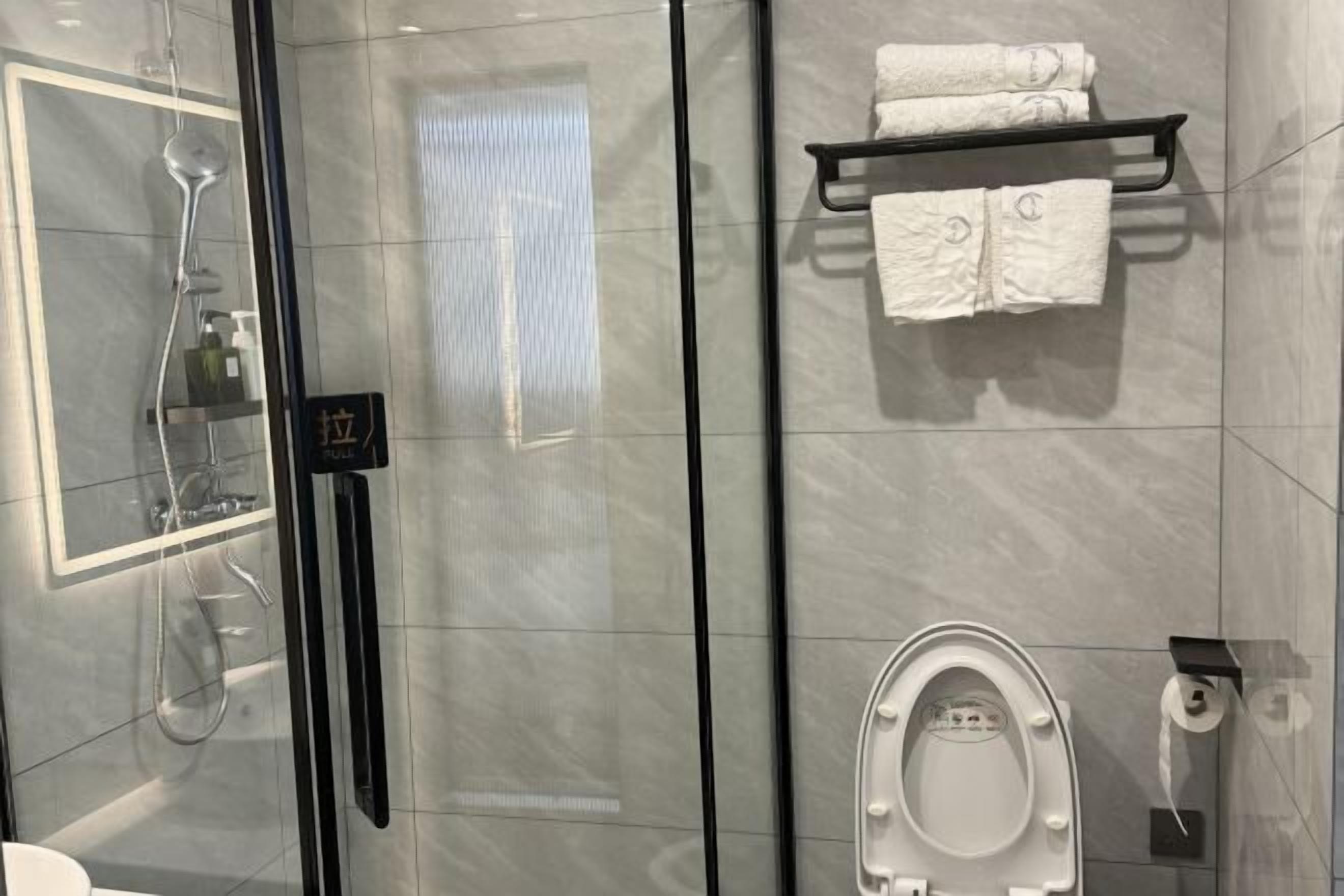 Une salle de bain moderne avec une douche à parois de verre, des toilettes et un porte-serviettes avec des serviettes pliées.