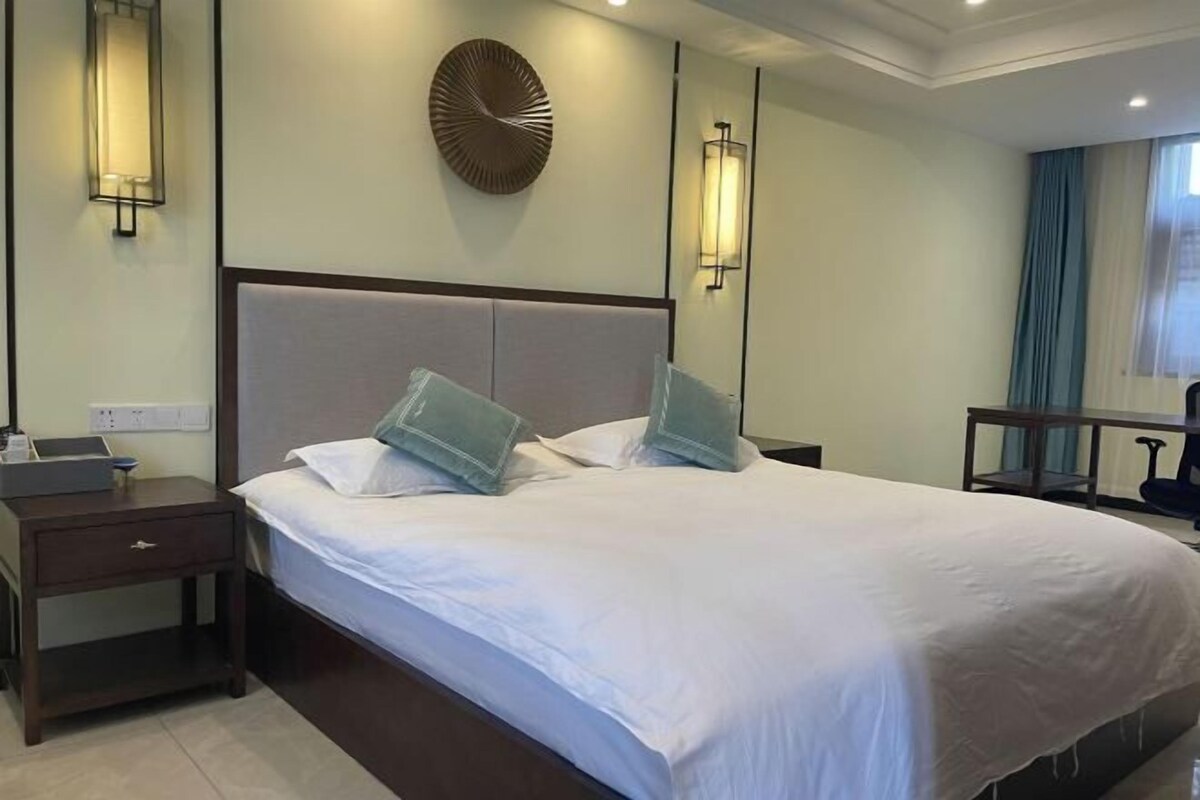 A hotel room with a large bed, bedside tables, a wall clock, and a mirror.