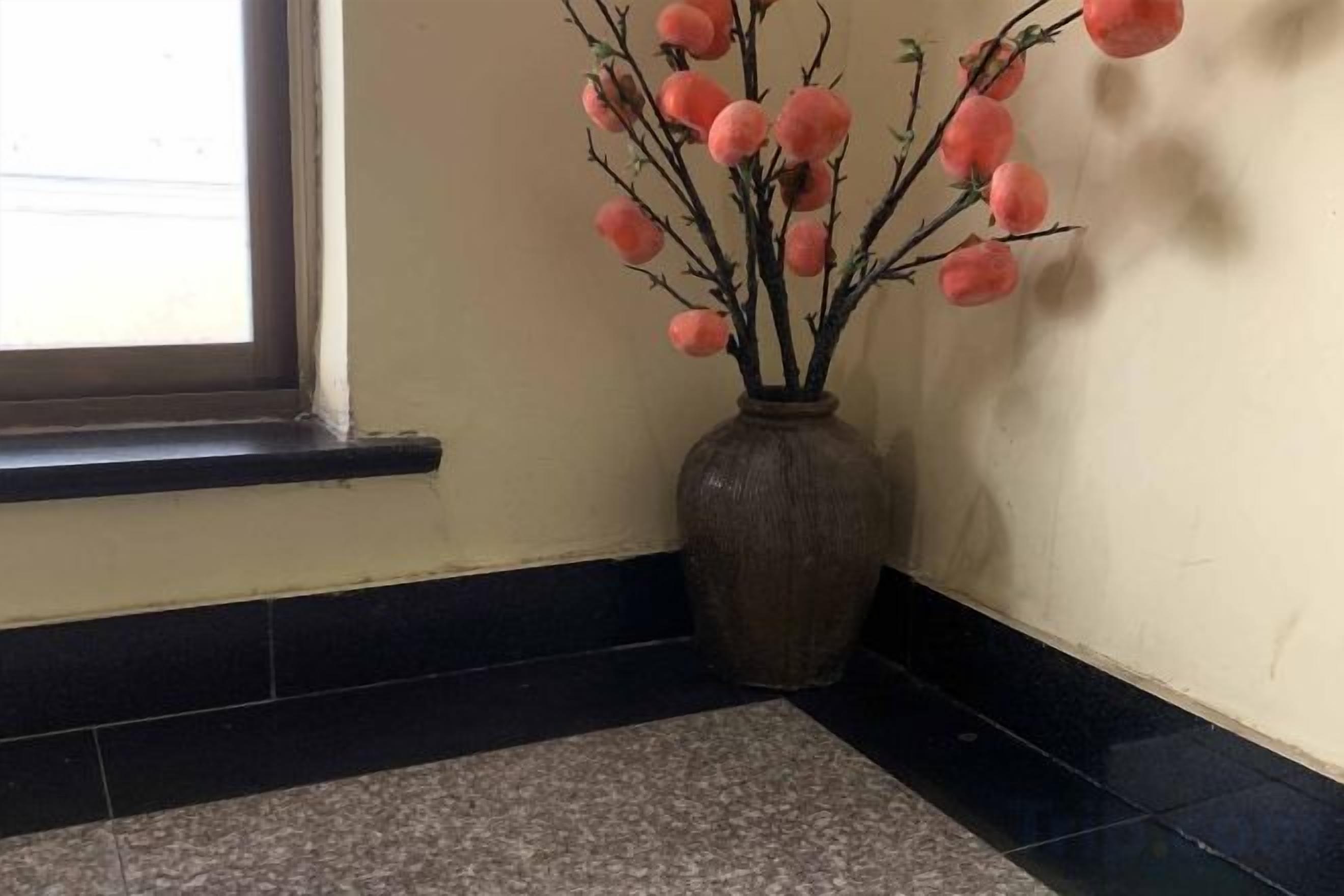 Eine Ecke mit einer Vase voller runder, pinkfarbener Dekorationen auf einem Fliesenboden.