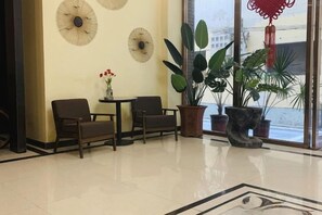 Un área de recepción con dos sillones, una mesa pequeña con flores y plantas grandes en macetas.