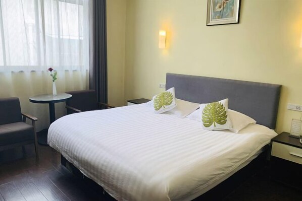 Una habitación de hotel con una cama, una silla, una mesita y una ventana con cortinas.