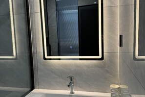 A modern bathroom with a large mirror, a sleek faucet, and a glass shower enclosure. - Qi Ting Hotel (Linquan)