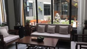 Una sala de estar moderna con un sofá, una mesa de centro y sillas. Se ve un gran ventanal que ofrece vistas al patio exterior con plantas y una escalera.