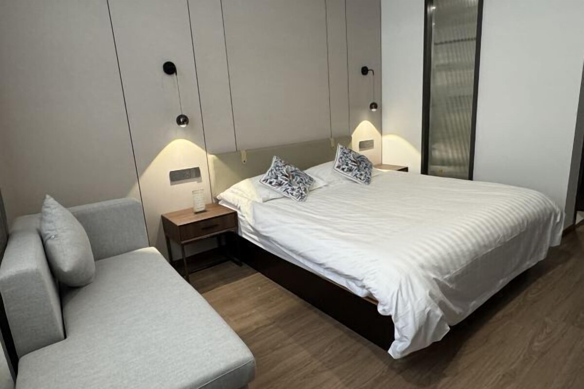 A modern bedroom with a bed, a grey sofa, and bedside tables with lamps.