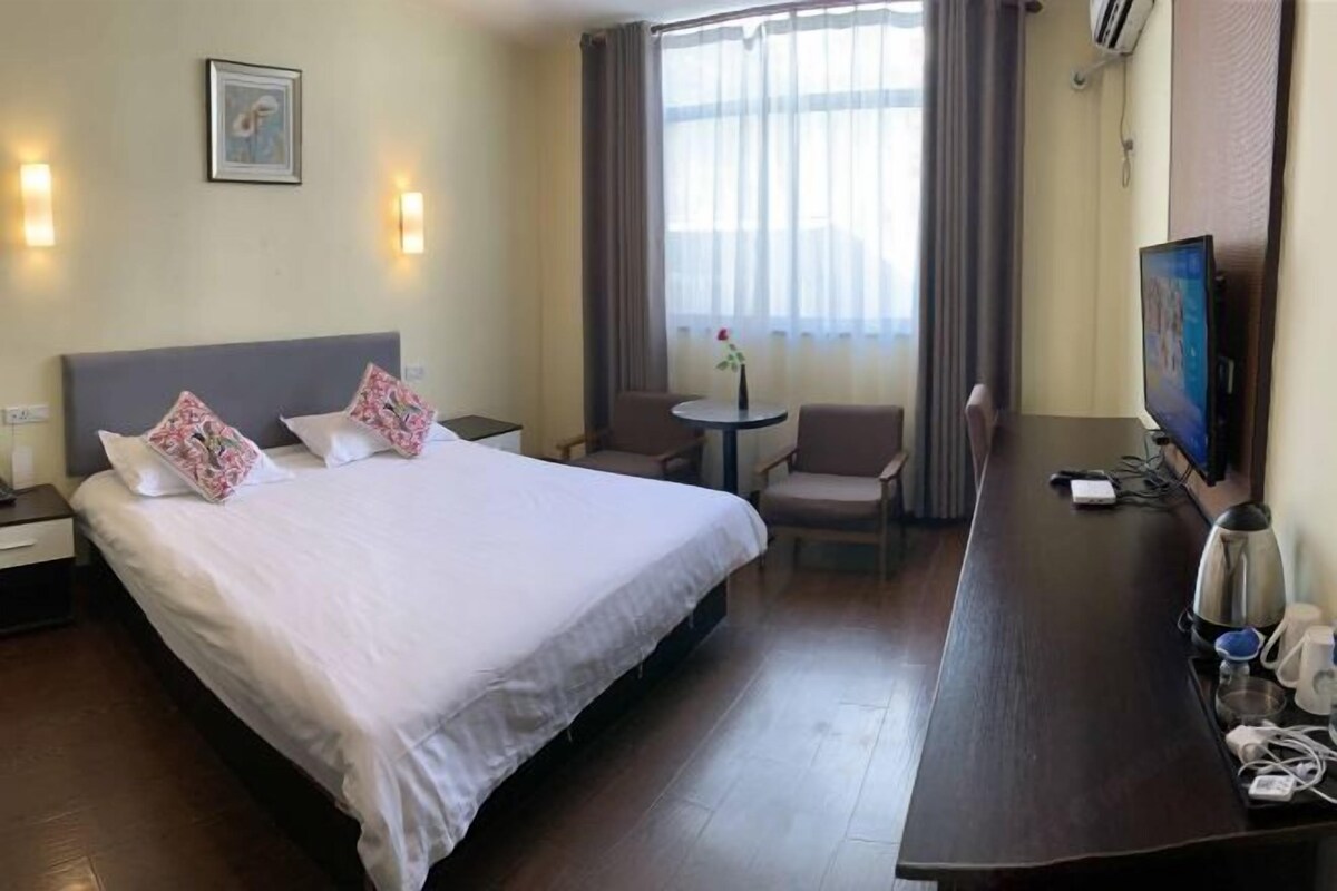 A hotel room with a bed, bedside table, TV, and a small seating area with a chair and table.