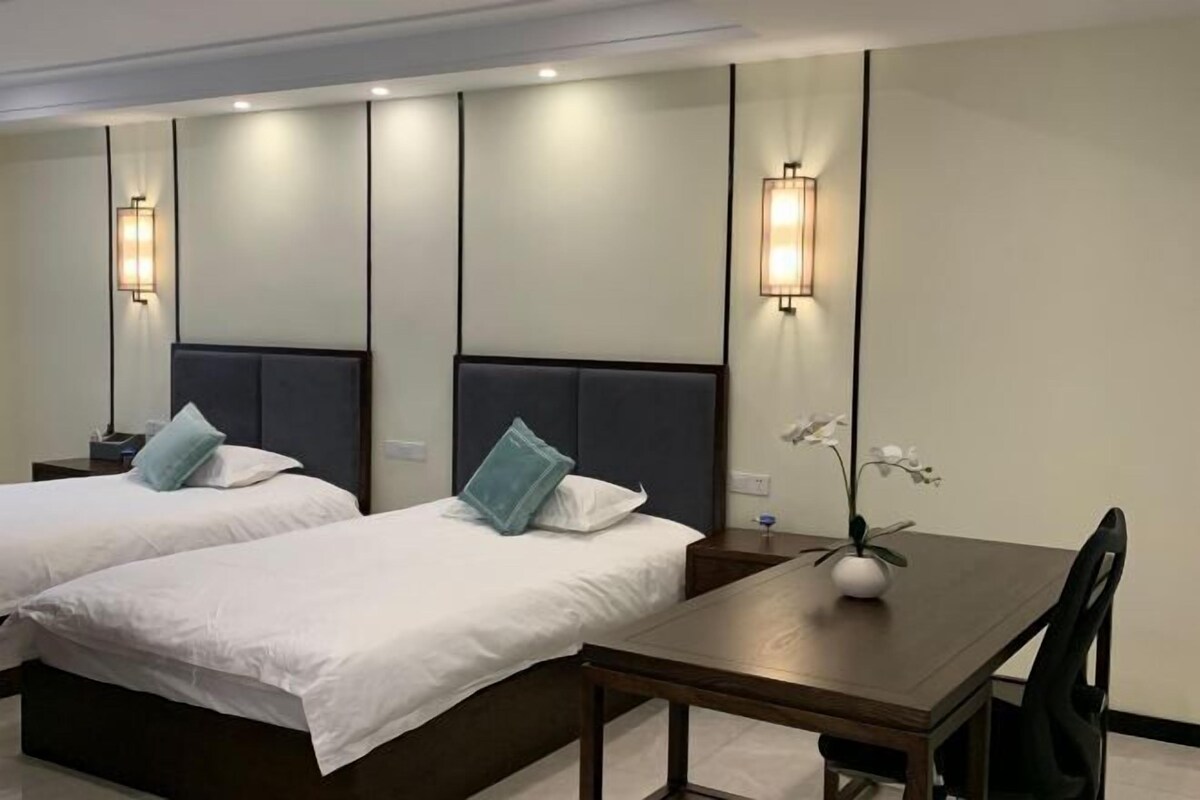 A hotel room with two beds, a wooden table, and wall-mounted lights.