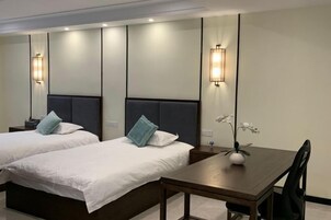 A hotel room with two beds, a wooden table, and wall-mounted lights.