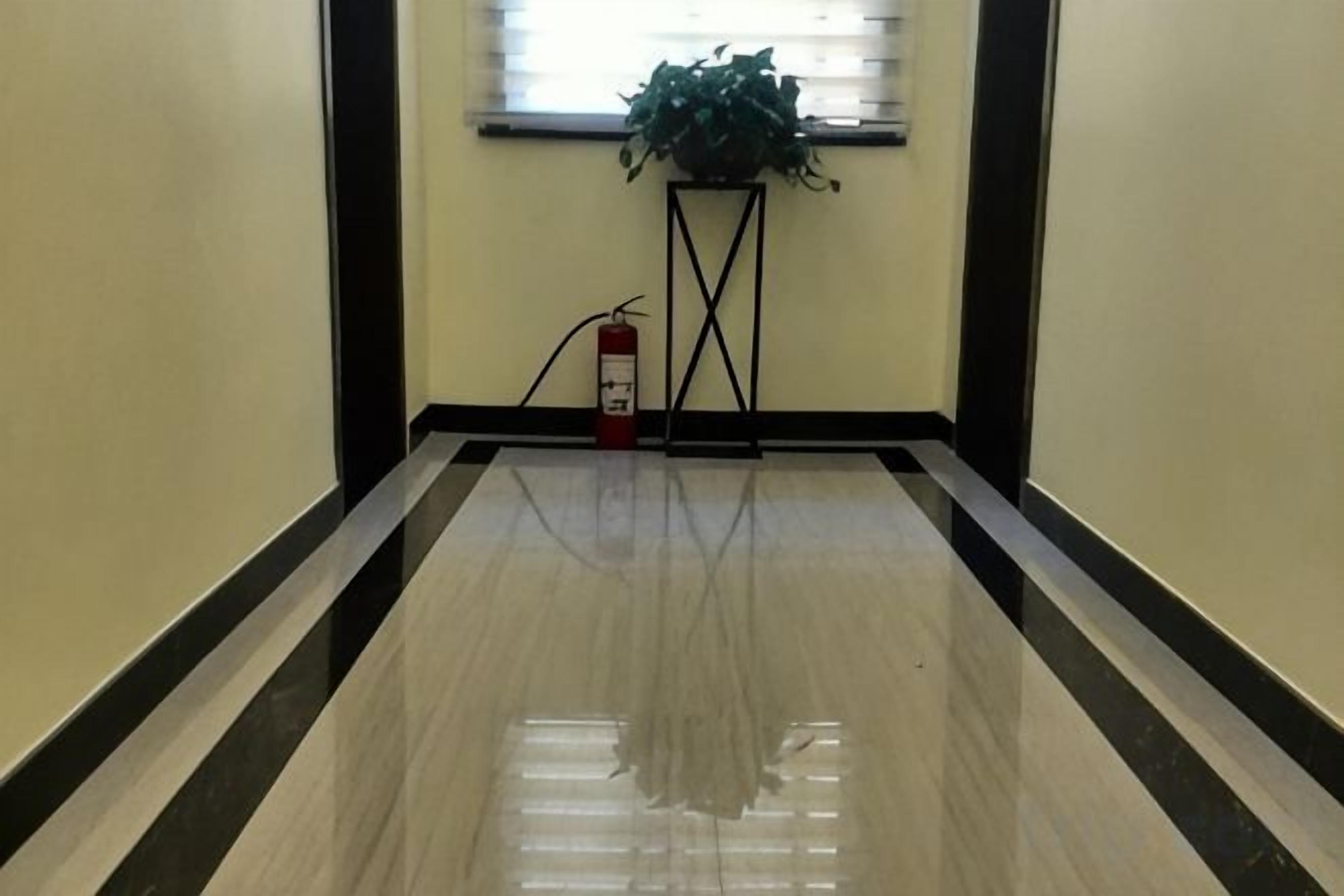Un pasillo con piso brillante, un extintor y una planta sobre un pedestal.