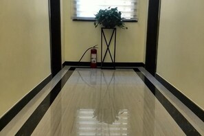 Un pasillo con piso brillante, un extintor y una planta sobre un pedestal.