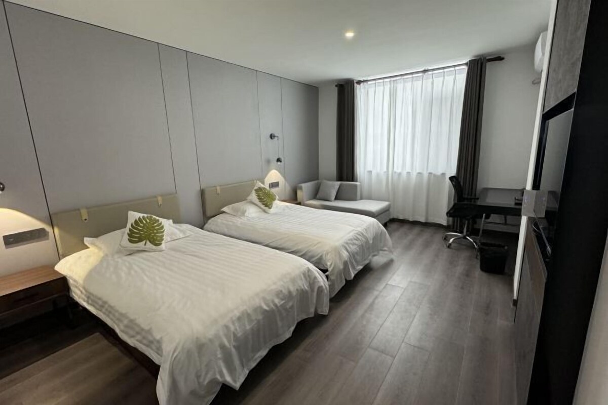 A hotel room with two beds, a desk, a chair, and a large window with curtains.