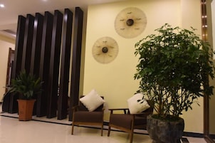 Un hall con dos sillones, una planta en maceta grande y ventiladores de pared decorativos.