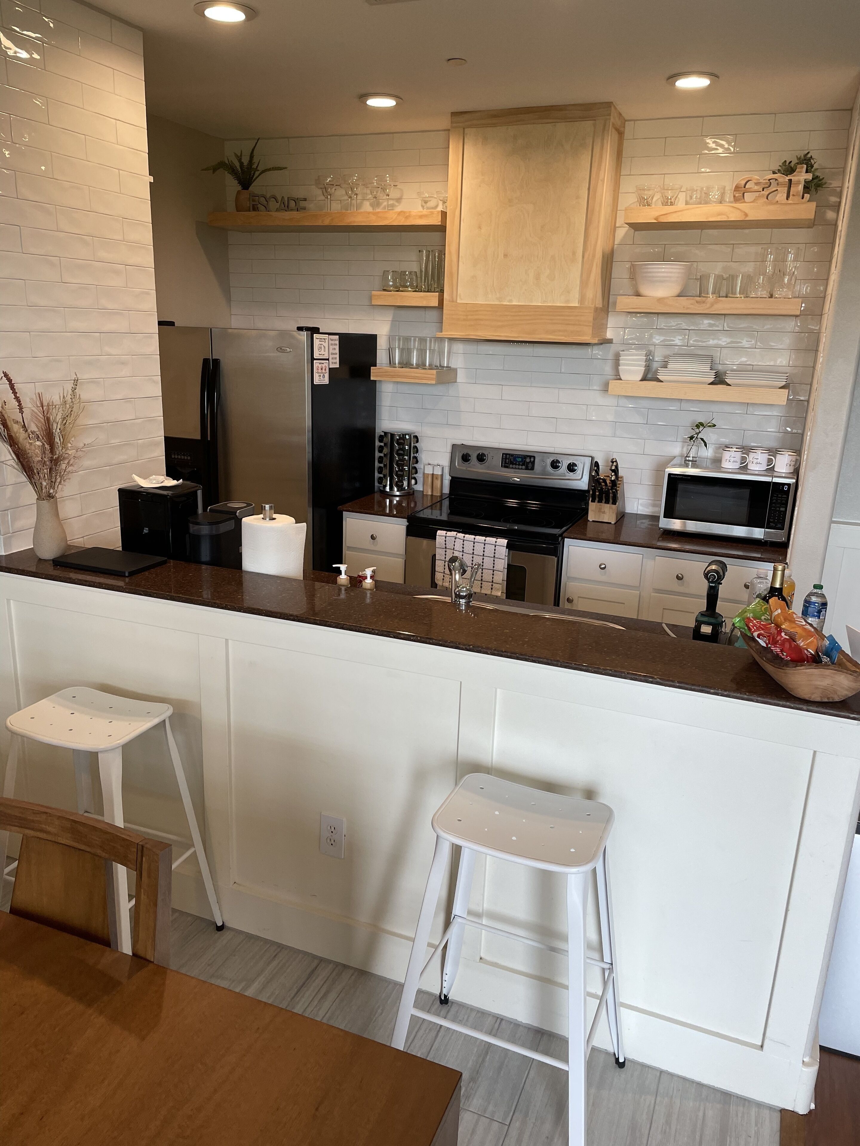 A modern kitchen with white cabinetry, stainless steel appliances, and a wooden island with stools.