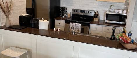 A modern kitchen with white cabinetry, stainless steel appliances, and a wooden island with stools.