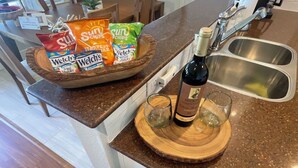 Un comptoir de cuisine avec un saladier en bois contenant des collations, une bouteille de vin et des verres.