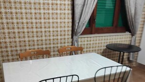 Una zona de menjador amb una taula blanca, quatre cadires de metall i un mur amb un disseny decoratiu.