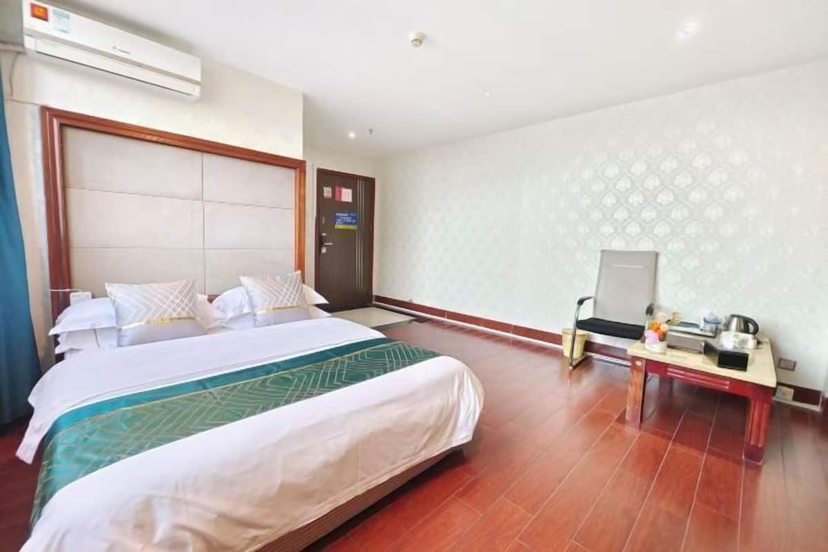 A hotel room with a large bed, a desk with a chair, an air conditioner, and a patterned wall.