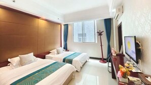 A hotel room with two beds, a desk with a TV, and a window with curtains.