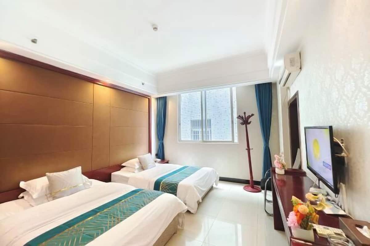 A hotel room with two beds, a desk with a TV, and a window with curtains.