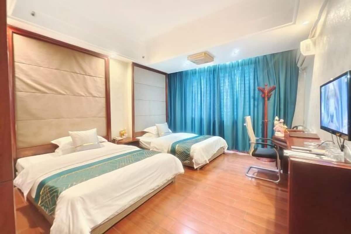 A hotel room with two beds, a desk with a computer, and a large window with blue curtains.