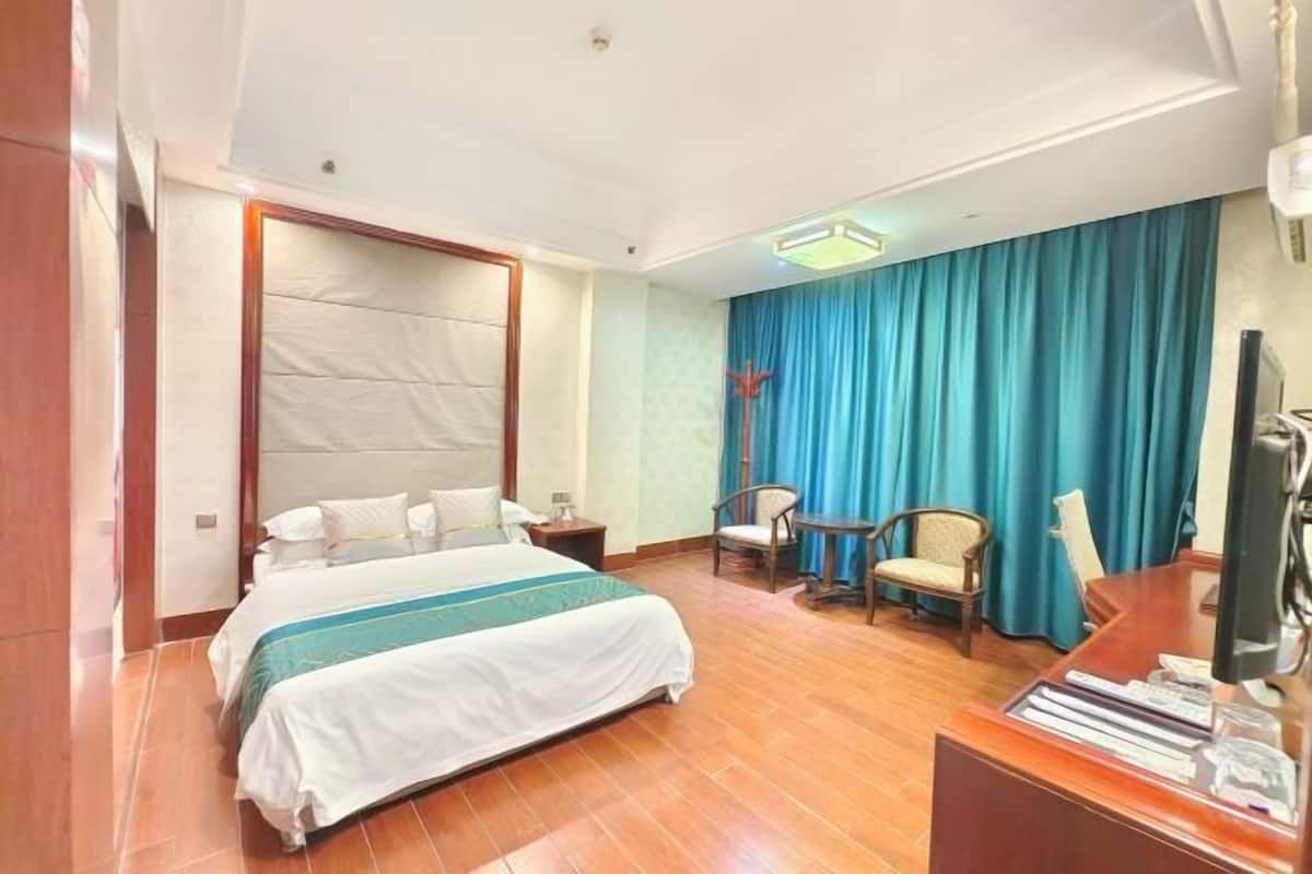 A hotel room with a bed, a desk, a chair, a television, and a curtain.