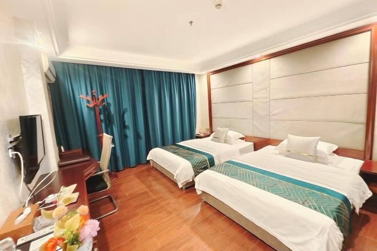 A hotel room with two beds, a desk, a chair, a TV, and a curtain.