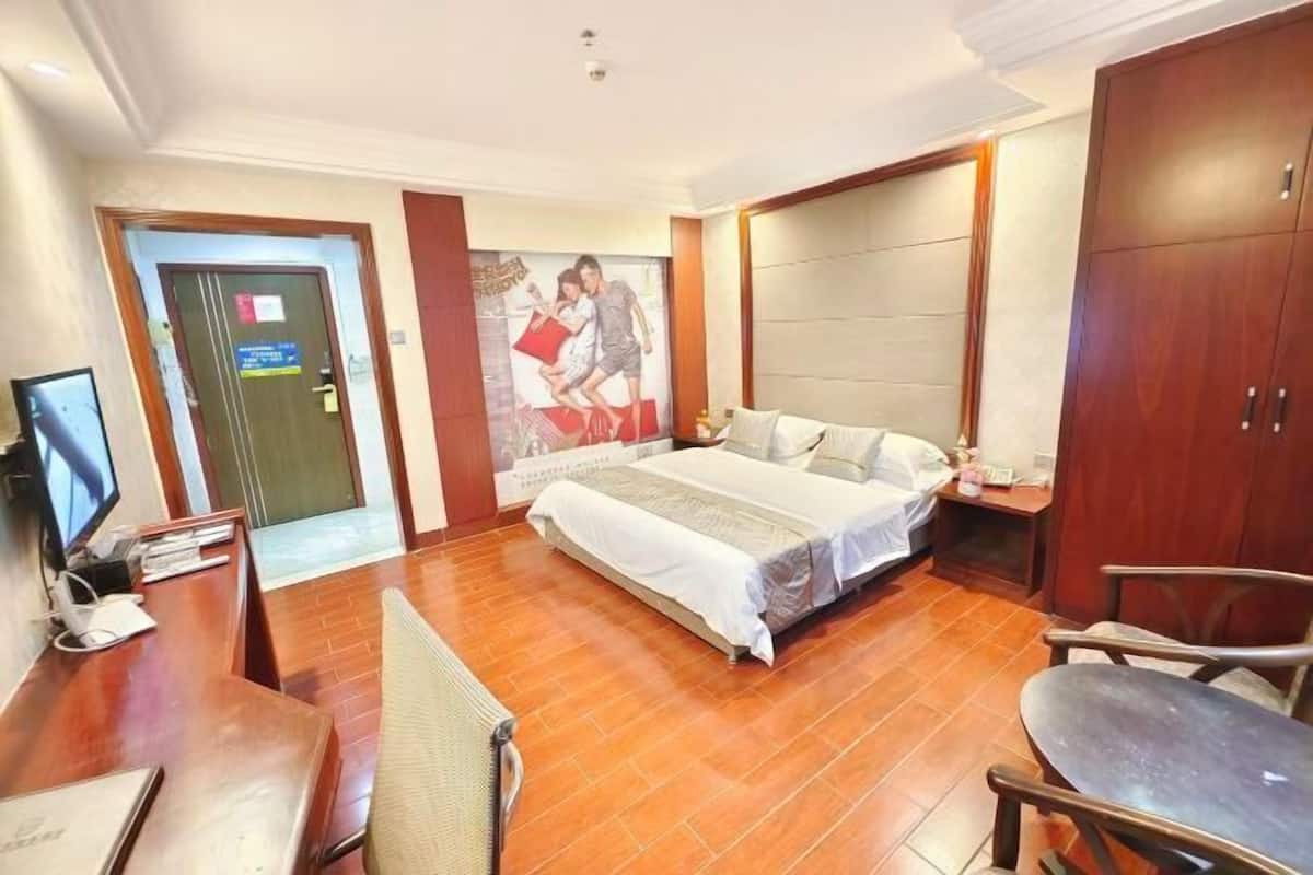 A hotel room with a bed, a desk with a computer, a chair, and a TV.