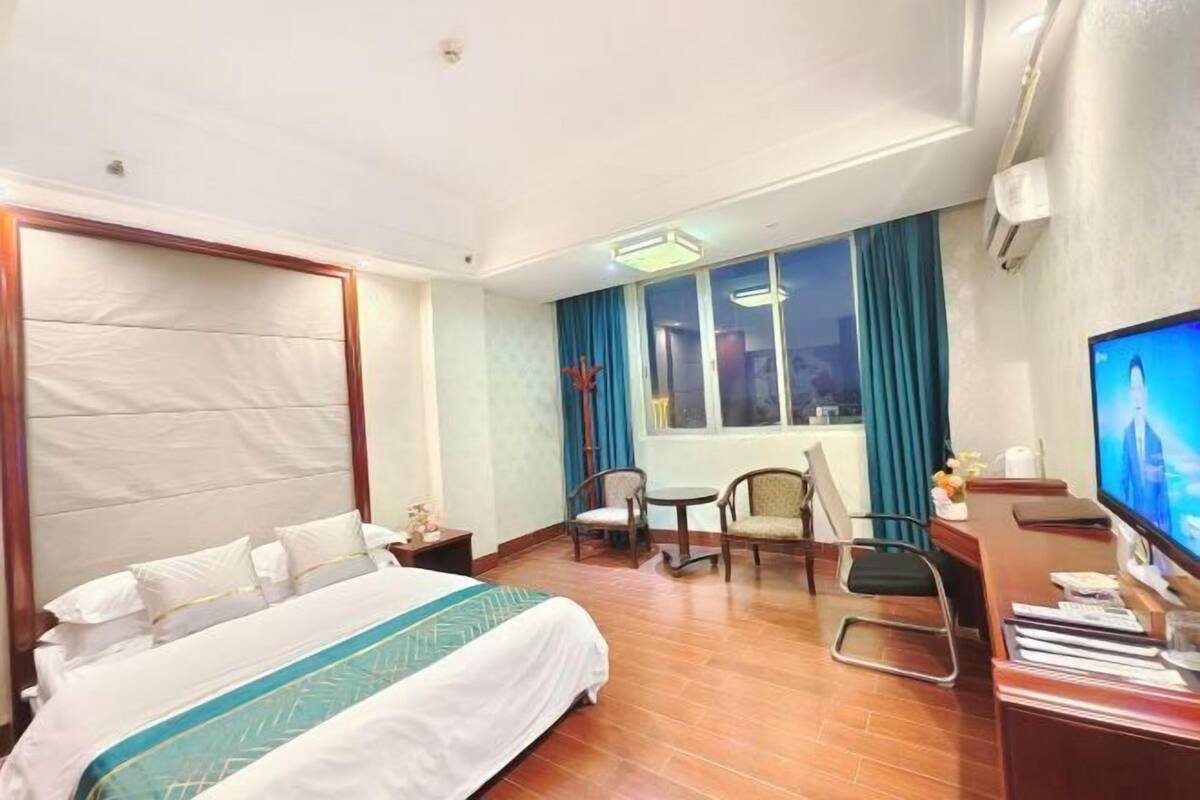 A hotel room with a bed, a desk, a chair, a television, and a window with curtains.