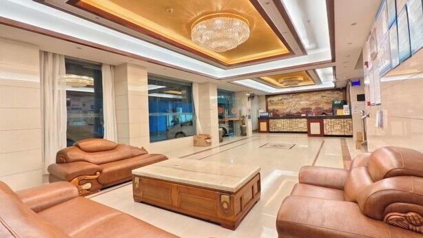 A spacious lobby with leather sofas, a marble coffee table, and a chandelier.