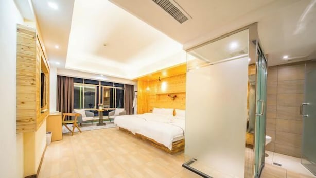 Habitación de hotel moderna con cama, un área de descanso pequeña, cabina de ducha de vidrio y una pared decorativa de madera.