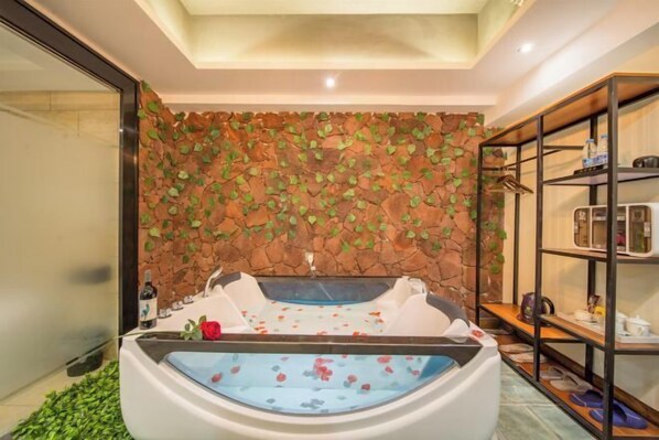 A spa room with a stone wall, a bathtub, and shelves with toiletries. - Sofia Hotel (Wenchang)