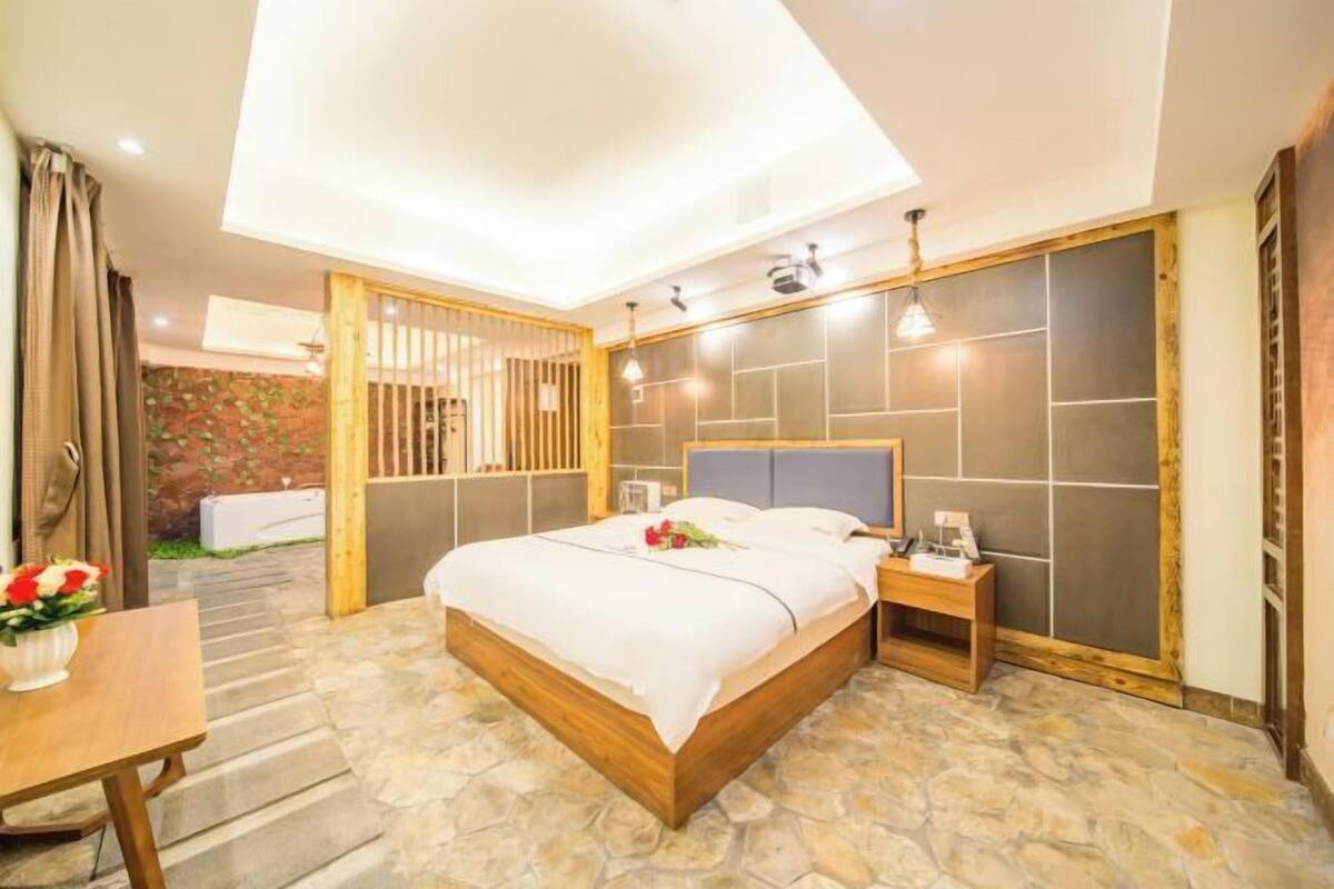 Quarto com cama, mesa de cabeceira e vista para o exterior.