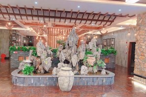 A lobby with a central rock formation, a reception desk, and a stone wall. - Sofia Hotel (Wenchang)