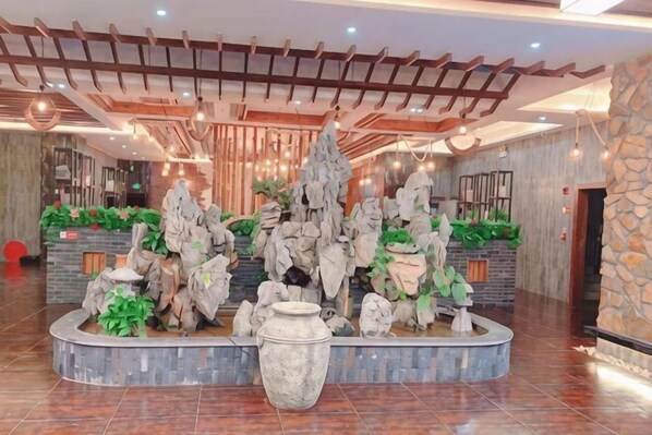 A lobby with a central rock formation, a reception desk, and a stone wall. - Sofia Hotel (Wenchang)