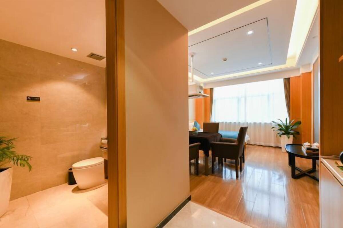 A modern hotel room with a wooden floor, a dining area with a table and chairs, and a visible toilet.