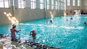 En inomhuspool med klart vatten, stora fönster och en poolkant som är skyddad med nät.