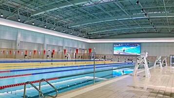 A swimming pool with lanes, a tiled floor, and a high ceiling with metal beams.