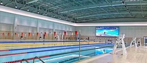 A swimming pool with lanes, a tiled floor, and a high ceiling with metal beams.