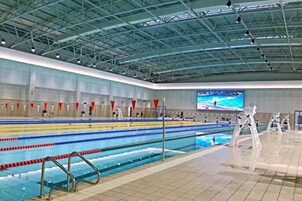 Una piscina con carriles, suelo de baldosas y techo alto con vigas metálicas.