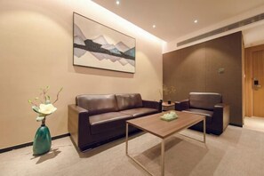 Eine moderne Hotelhalle mit einem braunen Ledersofa, einem Holztisch, einer Blumenvase und einem Gemälde an der Wand.