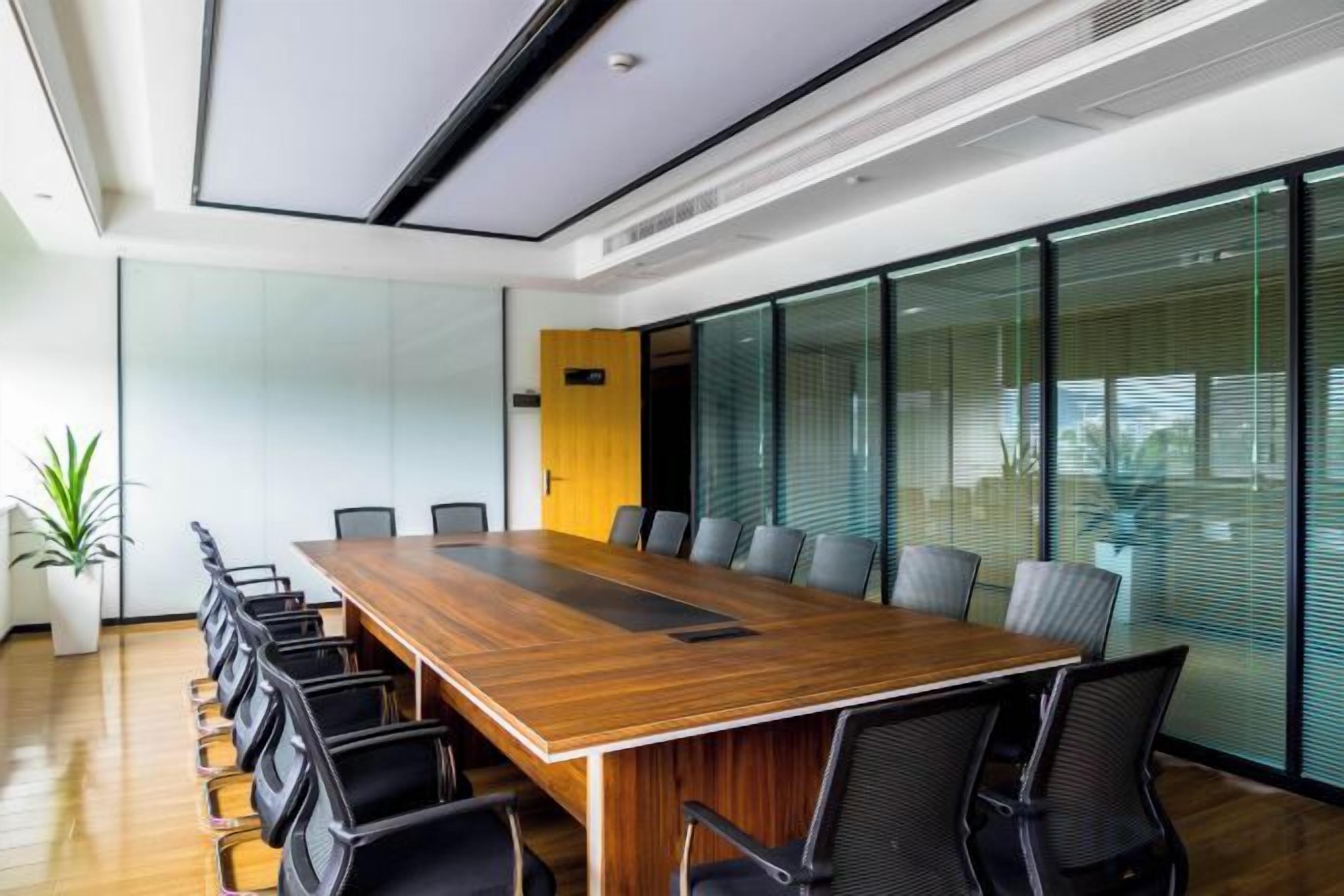 A conference room with a long wooden table, black chairs, and glass walls.