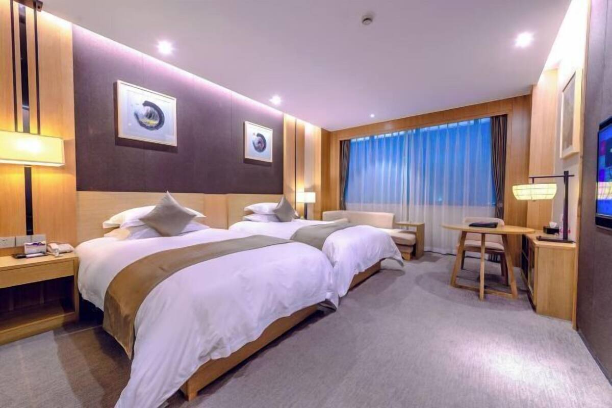 A hotel room with two beds, a desk, a chair, and a TV.