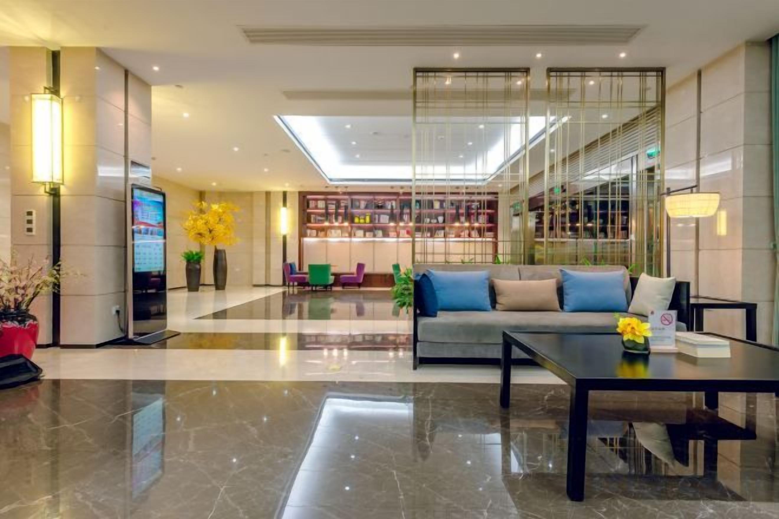 Un moderno vestíbulo de hotel con mostrador de recepción, zona de estar y una sala de lectura con paredes de vidrio.
