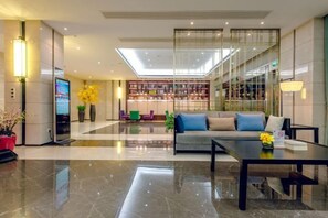Un moderno vestíbulo de hotel con mostrador de recepción, zona de estar y una sala de lectura con paredes de vidrio.