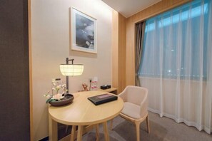 A hotel room with a round wooden table, a chair, a lamp, a framed picture on the wall, and a window with sheer curtains. - TaiYun Easeful Hotel (Linhai)