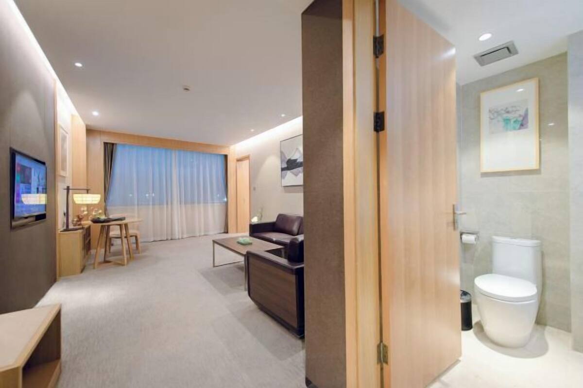 A modern hotel room with a living area, a sofa, a coffee table, and a TV.