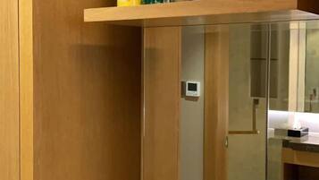 A wooden cabinet with a glass door, a small control panel, and a shelf above it.