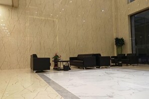 Eine Lobby mit Marmorwänden, schwarzen Sitzgelegenheiten, einem kleinen Tisch mit Pflanze und einem großen Fenster.