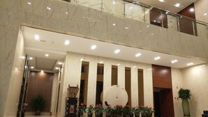 A lobby with a marble floor, a reception desk, potted plants, and a large decorative sphere. - Huangsheng Hotel (Wuchuan)