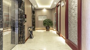 A hotel corridor with a marble floor, a potted plant, and a wall-mounted information board. - Huangsheng Hotel (Wuchuan)