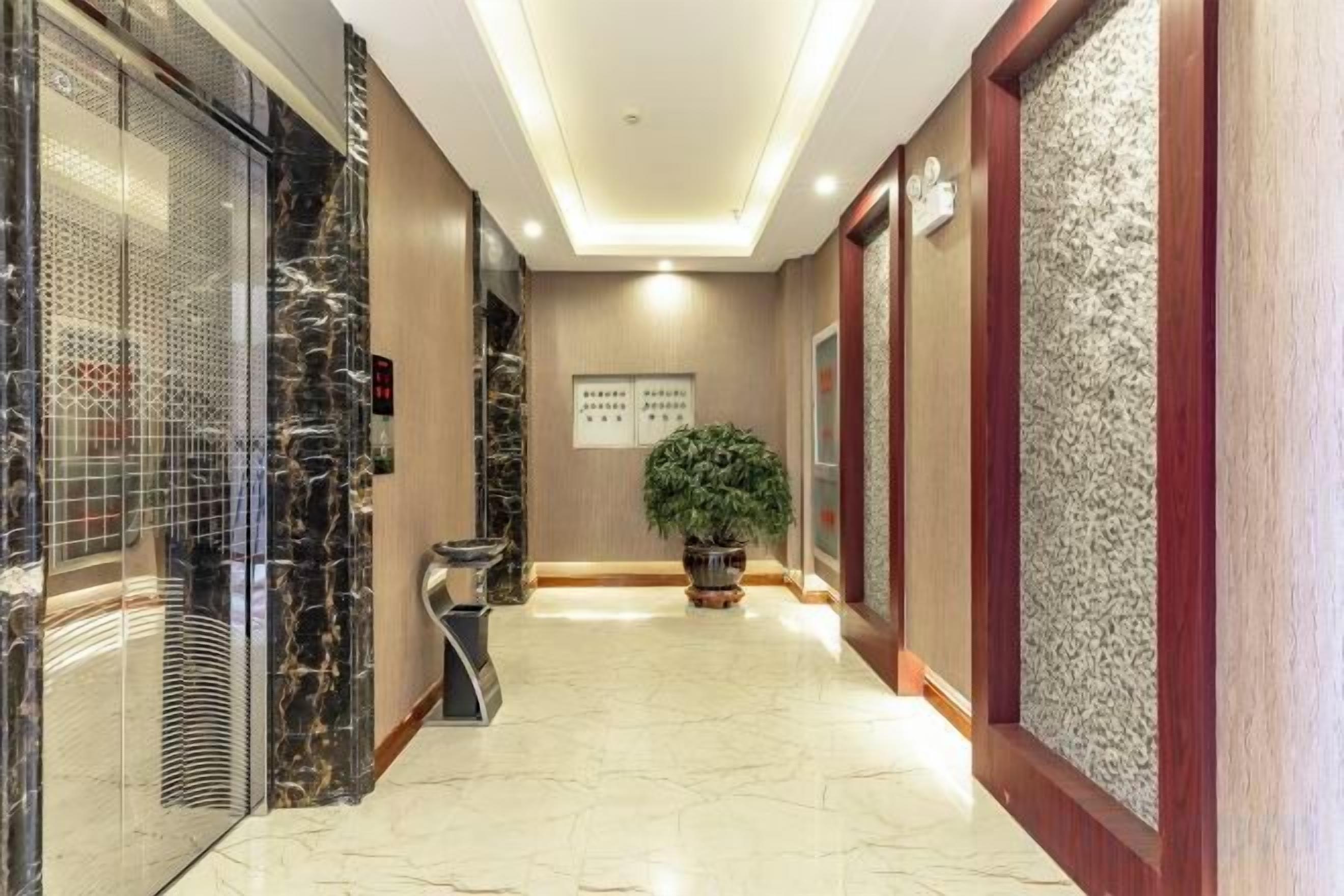 A hotel corridor with a marble floor, a potted plant, and a reception desk.